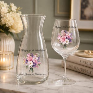 May include: A clear glass carafe and a matching wine glass, both featuring a printed bouquet of pink and purple flowers. The carafe is inscribed with "Happy 90th Birthday" and "Love James & Gemma xx," while the wine glass displays "Happy 90th Birthday."
