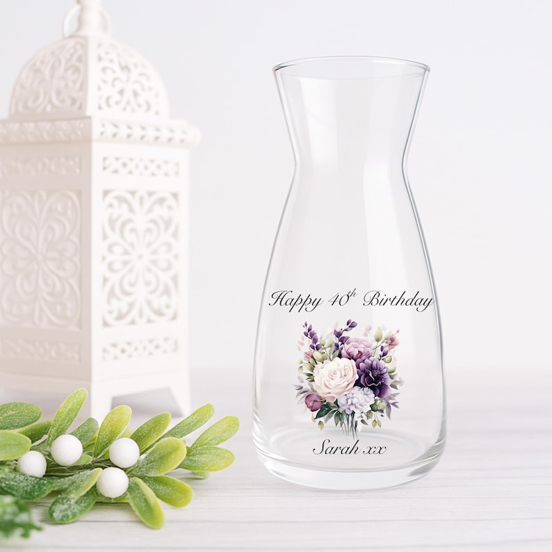 Pode incluir: Um vaso de vidro transparente com um design de buqu&ecirc; floral. O vaso tem o texto "Happy 40th Birthday" e "Sarah xx". O buqu&ecirc; apresenta flores roxas, brancas e rosas. Uma lanterna branca e vegeta&ccedil;&atilde;o est&atilde;o no fundo.