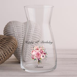 Pode incluir: Uma jarra de vidro transparente com uma base larga e um gargalo estreito. A jarra &eacute; decorada com um buqu&ecirc; floral em tons de rosa e roxo, e o texto "Happy 16th Birthday Danni".