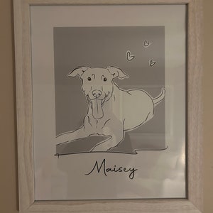 May include: A framed black and white line drawing of a dog with the name "Maisey" written below. The background is a light gray with small hearts scattered around the dog.