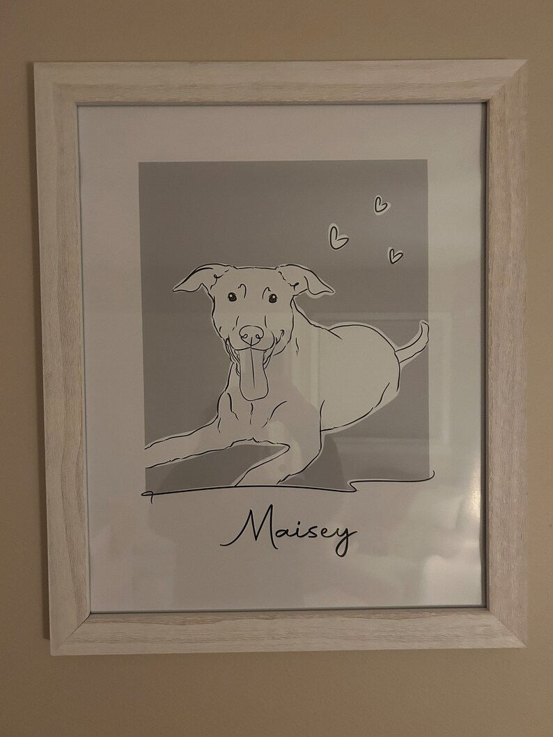 May include: A framed black and white line drawing of a dog with the name "Maisey" written below. The background is a light gray with small hearts scattered around the dog.