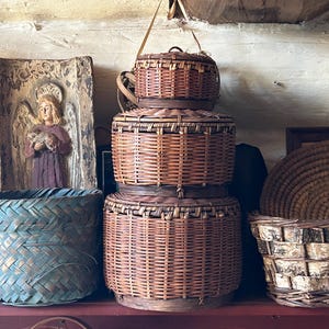 May include: A set of three brown wicker baskets stacked on top of each other. The baskets are woven with a natural brown material and have a rustic look. The baskets are sitting on a wooden shelf.