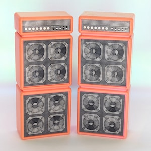 May include: Two orange toy amplifiers stacked, each with a top section featuring a series of small, round lights and a control panel. The main body has four square speaker grilles with a circular design. The background is a light, gradient color.