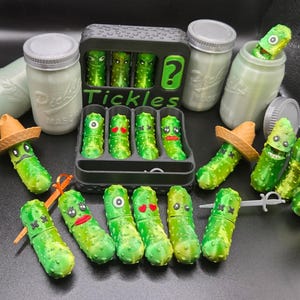 May include: A collection of novelty pickle-shaped containers with various facial expressions and accessories. Some pickles are in a black tray, others are in mason jars. The word "Tickles" is printed on a black container.
