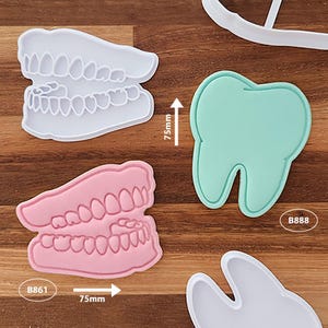 May include: A set of plastic cookie cutters in the shapes of teeth and dentures. The white and pink denture cutters measure 75mm in height. A mint green tooth cutter is labelled B888, and a white tooth cutter is partially visible.