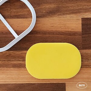 May include: A yellow fondant oval shape on a wooden surface. The oval is slightly raised and has a smooth texture.