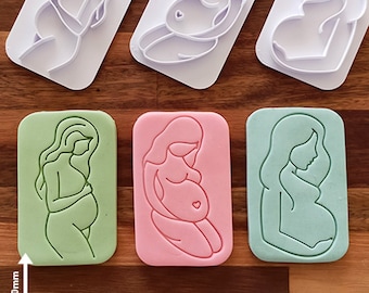 Può includere: Tre stampini per biscotti a forma di donna incinta. Gli stampini sono in plastica bianca e misurano 80 mm per 50 mm. Gli stampini sono su una superficie di legno. Gli stampini sono per fare biscotti o pasta di zucchero.