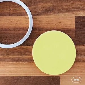 May include: A yellow circle cookie cutter on a wooden surface. The cutter is made of plastic and is about 7.5 cm in diameter. B046