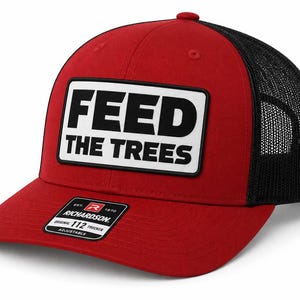 May include: Red and black trucker hat with the text "FEED THE TREES" in a white rectangle. The hat has a curved brim and a mesh back. The Richardson 112 Trucker hat is adjustable.