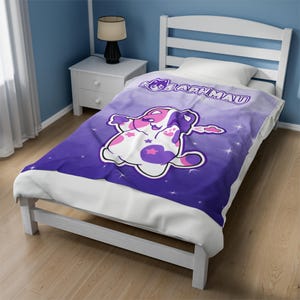 May include: Purple and white fleece throw blanket with a cartoon cat wearing a pink and purple star-shaped outfit. The blanket has a gradient background with white stars and the text "Aphmau" in white.