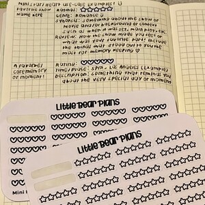 May include: Two sheets of white sticker paper with black hearts and stars printed on them. The top sheet has rows of hearts and the bottom sheet has rows of stars. The text "Little Bear Plans" is printed on both sheets.