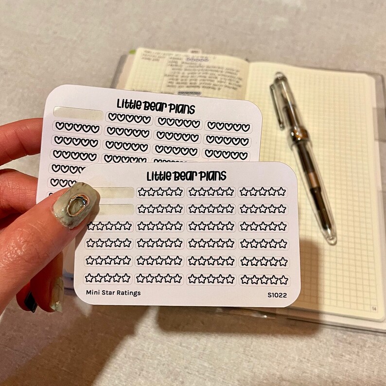 May include: Two sheets of white sticker paper with black outlines of hearts and stars. The top sheet has the text "Little Bear Plans" and the bottom sheet has the text "Little Bear Plans" and "Mini Star Ratings". The bottom sheet also has the text "S1022".