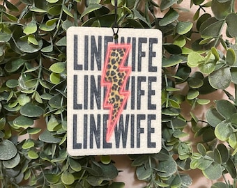 May include: A white car air freshener with the text "LINEWIFE" repeated three times in black. A pink and black leopard print lightning bolt is in the center of the air freshener.