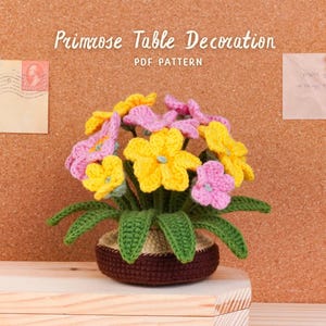 May include: A crocheted primrose table decoration in a brown pot. The flowers are yellow and pink, with green leaves. The text "Primrose Table Decoration PDF Pattern" is visible.