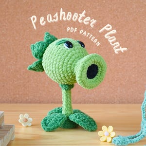 Può includere: Un modello di uncinetto per un personaggio del videogioco, Peashooter Plant, di Plants vs. Zombies. Il giocattolo all'uncinetto è di colore verde.