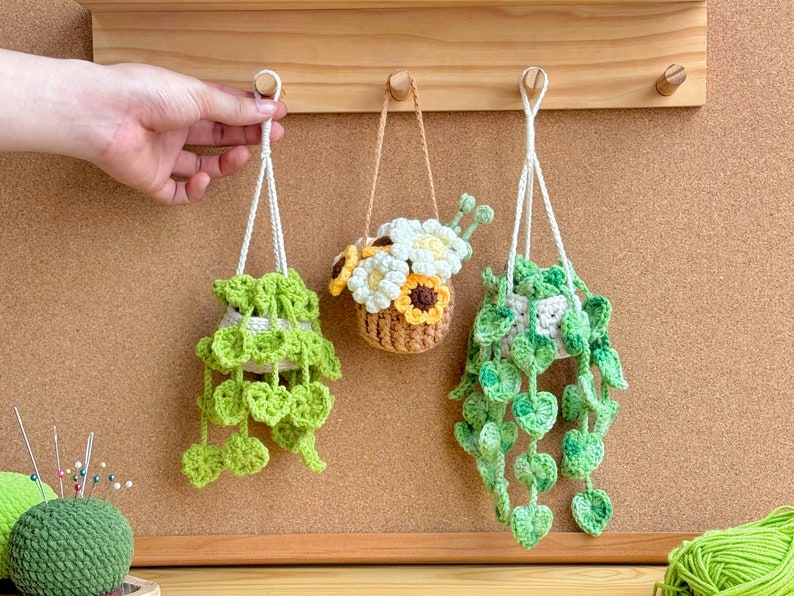 May include: Three crocheted hanging planters with white string. One planter has a crocheted flower arrangement with white and yellow flowers. The other two planters have green crocheted leaves.