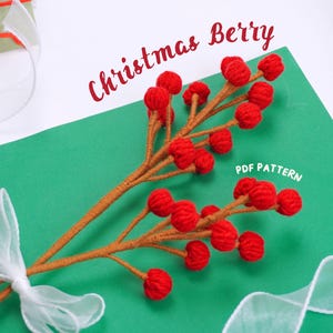 May include: A close-up of a handmade Christmas berry sprig with red felt berries and brown yarn stems. The sprig is tied with a white ribbon and the text "Christmas Berry PDF Pattern" is visible in the image.