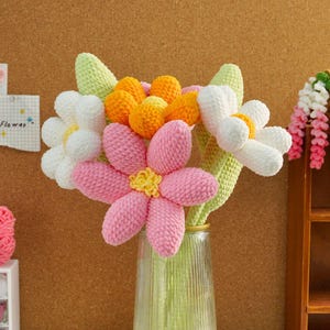 May include: A bouquet of crocheted flowers in a clear glass vase. The flowers are pink, white, and orange. The stems are green.