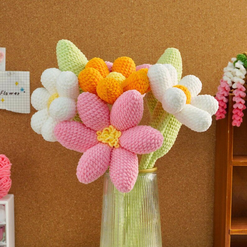 May include: A bouquet of crocheted flowers in a clear glass vase. The flowers are pink, white, and orange. The stems are green.