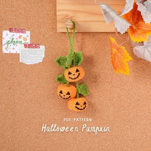 Op de afbeelding: Een handgemaakte gehaakte Halloween pompoen decoratie met drie oranje pompoenen, groene bladeren en lachende jack-o'-lantern gezichten. De tekst "PDF PATTERN Halloween Pumpkin" is zichtbaar. De achtergrond is een prikbord.