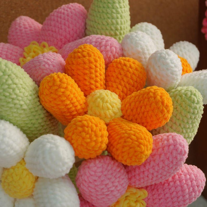 May include: A crocheted flower bouquet with pink, white, orange, yellow, and green yarn flowers. The flowers are arranged in a circular pattern.