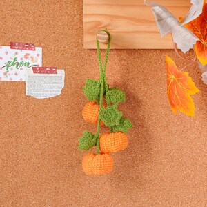 May include: A handmade crochet pumpkin garland with three orange pumpkins and green leaves. The garland is hanging against a corkboard background, perfect for fall decor. The pumpkins are approximately 2 inches in diameter.