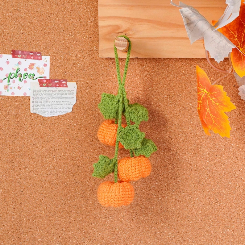 May include: A handmade crochet pumpkin garland with three orange pumpkins and green leaves. The garland is hanging against a corkboard background, perfect for fall decor. The pumpkins are approximately 2 inches in diameter.
