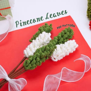 May include: A bunch of crocheted pine cone leaves in green and white, tied together with brown stems and a white ribbon. The leaves are arranged on a red background with the text "Pinecone Leaves PDF Pattern" above them.