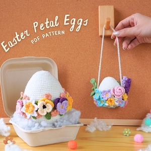 Könnte beinhalten: Zwei gehäkelte Ostereier, die mit bunten Blumen verziert sind. Ein Ei befindet sich in einem weißen Pappbehälter, das andere hängt an einem Holzhaken. Der Text "Easter Petal Eggs PDF Pattern" ist auf einer Korktafel geschrieben.