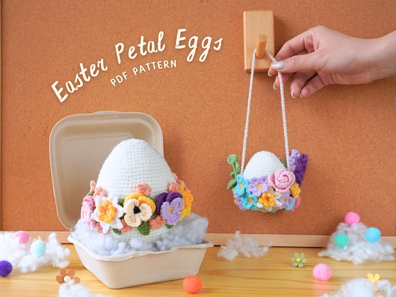 May include: Two crocheted Easter eggs decorated with colorful flowers. One egg is in a white cardboard container, and the other is hanging from a wooden hook. The text "Easter Petal Eggs PDF Pattern" is written on a corkboard.