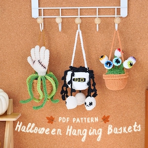 May include: Three crocheted Halloween hanging baskets. The first basket is a green plant with a white hand sticking out of the top. The second basket is a white mummy with black hair and eyes. The third basket is a green plant with colorful eyes sticking out of the top.  PDF PATTERN Halloween Hanging Baskets
