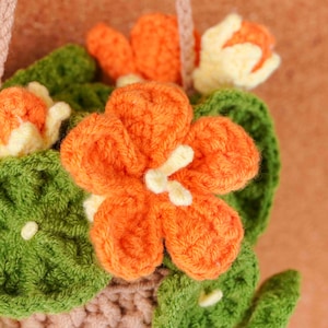 May include: Close-up of a handmade crochet flower arrangement. The arrangement features vibrant orange flowers with white centers, surrounded by green leaves. The crochet work is detailed, showcasing the texture of the yarn. The overall theme is floral and handmade.