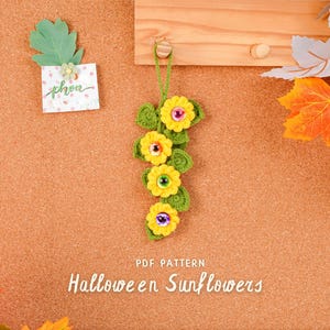 May include: A handmade crochet Halloween decoration featuring yellow sunflowers with googly eyes and green leaves. The text "Halloween Sunflowers" is displayed below the flowers. A small note with the word "phen" is pinned to the corkboard.