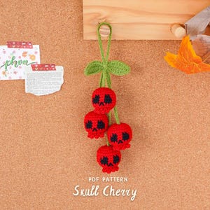 May include: A handmade crochet Skull Cherry decoration. The cherries are bright red with black skull faces, green leaves, and a green stem. The text "Skull Cherry" is visible below the cherries.