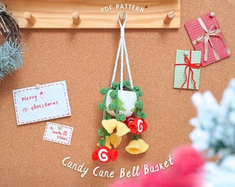 May include: A handmade crochet Candy Cane Bell Basket, featuring a white and green hanging planter with a Christmas tree design. The basket is adorned with red and yellow bell-shaped ornaments. The image includes the text "Merry Christmas".