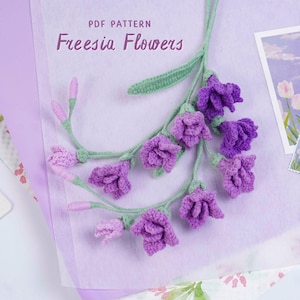 May include: A crochet pattern for Freesia Flowers is displayed, featuring a sprig of purple crocheted flowers with green stems and leaves. The text "PDF PATTERN Freesia Flowers" is visible. A postcard with a floral design is also present.