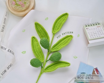 May include: A crocheted olive branch with green leaves and olives. The branch is on a white surface with the text "PDF PATTERN" written on it.