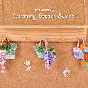 May include: A wooden shelf with three decorative, crocheted baskets hanging below. The baskets are filled with colorful flowers and foliage. The text "PDF PATTERN Cascading Garden Baskets" is above the shelf.