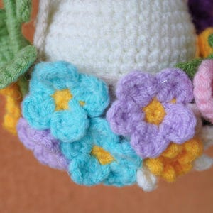 May include: A crocheted wreath with a white center and colorful flowers. The flowers are blue, purple, yellow, and pink.