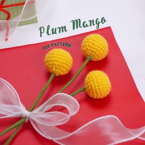 May include: Three yellow crocheted flowers with green stems on a red background with a white ribbon. The text "Plum Mango PDF PATTERN" is visible in the image.