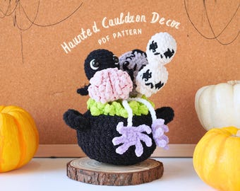 May include: A crocheted cauldron with a pink brain, green leaves, and purple tentacles. The cauldron is decorated with two white crocheted ghosts with black eyes. The cauldron is sitting on a wooden base. Haunted Cauldron Decor PDF Pattern.