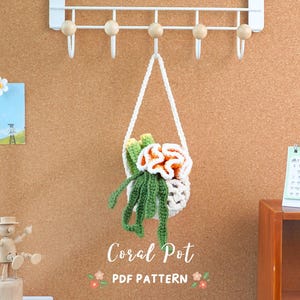 Peut inclure: Un modèle de crochet pour un pot de corail suspendu. Le modèle s'appelle "Coral Pot PDF Pattern". Le pot est blanc avec du corail vert et orange à l'intérieur.
