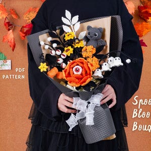 May include: A handmade crochet bouquet with a Halloween theme. The bouquet features orange and yellow flowers, black accents, and a gray cat. The bouquet is wrapped in gray paper and tied with a white ribbon. The text "Spooky Bloom Bouquet" is visible.