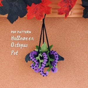 May include: A crochet hanging plant holder featuring a purple octopus with black spots and green leaves, suspended by black yarn. The text "PDF PATTERN Halloween Octopus Pot" is printed in white on the left side of the image.
