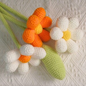 May include: A bouquet of crocheted flowers with orange, white, and yellow petals. The stems are green and the flowers are arranged in a bunch.