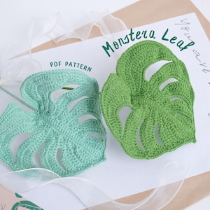 May include: Two crocheted Monstera leaf patterns, one in light green and the other in a darker green, are displayed on a white surface. The text "PDF PATTERN" is visible. The words "Monstera Leaf" are written in green script.