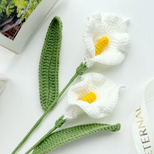 May include: Two white crocheted calla lilies with yellow centers and green crocheted leaves.