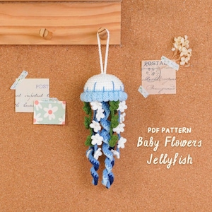 May include: A handmade crochet jellyfish ornament with a white and blue cap, blue and white tentacles, and small white flower accents. The text "PDF PATTERN Baby Flowers Jellyfish" is visible. The ornament hangs from a white string.