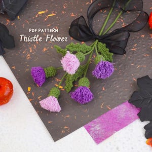 May include: A crochet thistle flower bouquet featuring four purple and light pink thistle heads with green stems and leaves, tied together with a black sheer ribbon. The text PDF PATTERN Thistle Flower is printed in white on the image.