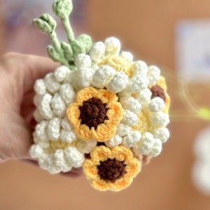 Op de afbeelding: Een gehaakt boeket van witte en gele bloemen. Het boeket bevat kleine witte bloemen en grotere gele bloemen met bruine centra.